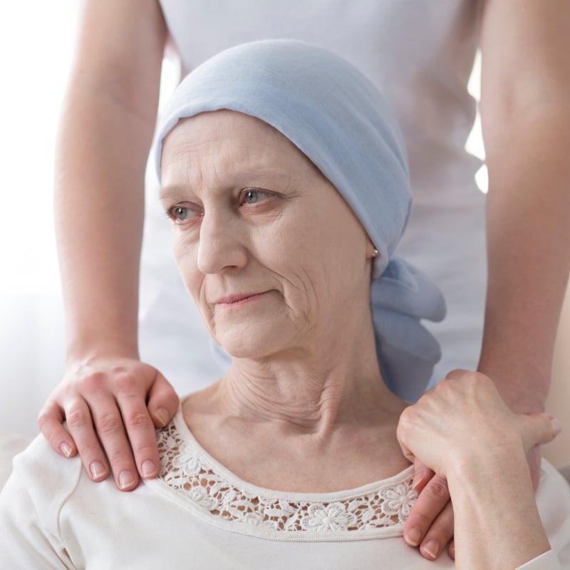 Crying elderly woman with cancer and a volunteer taking care of her